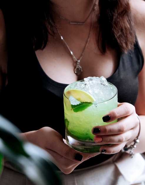 Foto gratuita la ragazza tiene un bicchiere di mojito con limone e menta