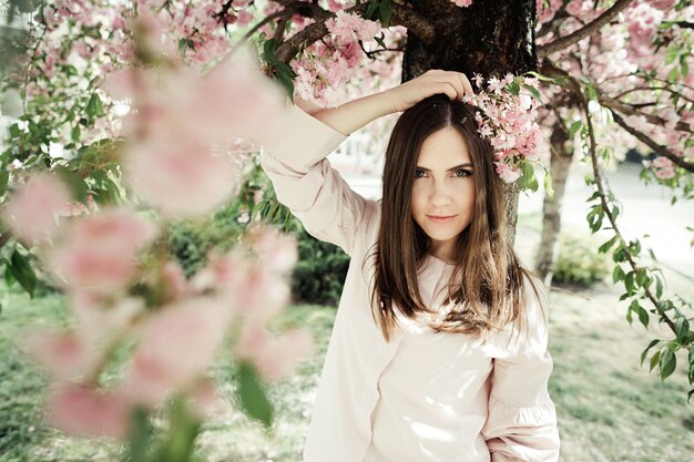 Girl holds hand behind her head with sakura branch and she stands near a sakura tree