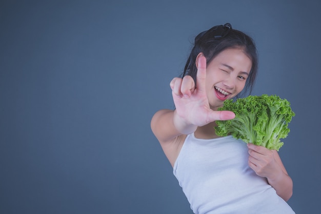 女の子は灰色の背景に野菜を保持します。