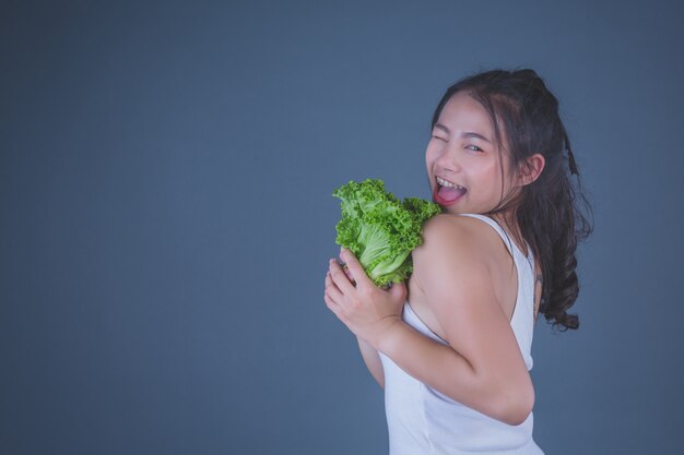Девушка держит овощи на сером фоне.