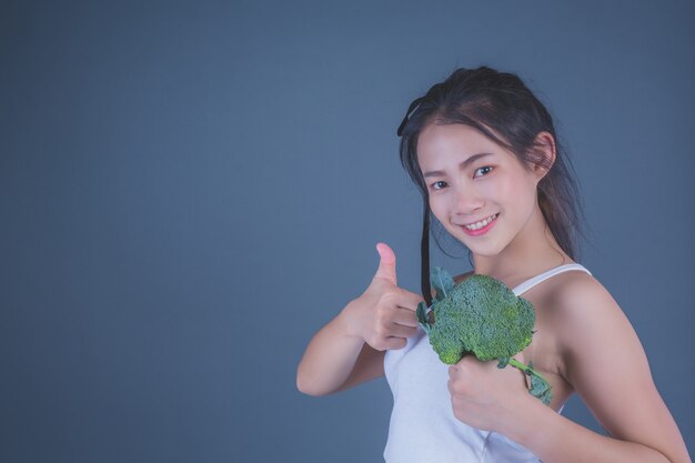 女の子は灰色の背景に野菜を保持します。
