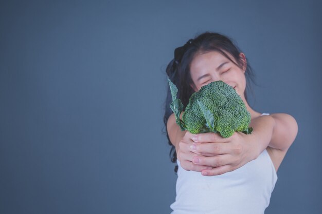 Девушка держит овощи на сером фоне.