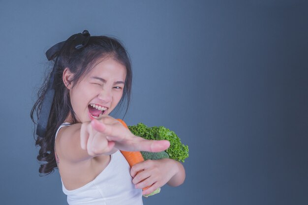 女の子は灰色の背景に野菜を保持します。