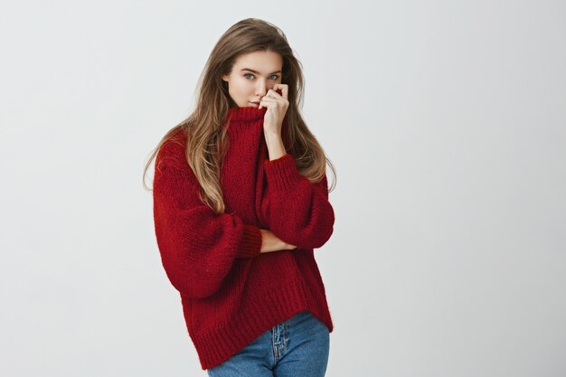 Girl hugged boyfriend and smells his perfume on her sweater. Portrait of sensual good-looking european model in trendy outfit pulling collar on face while standing against gray background.