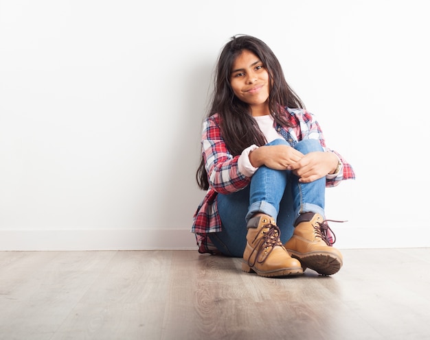 Ragazza che abbraccia le gambe, seduta sul pavimento