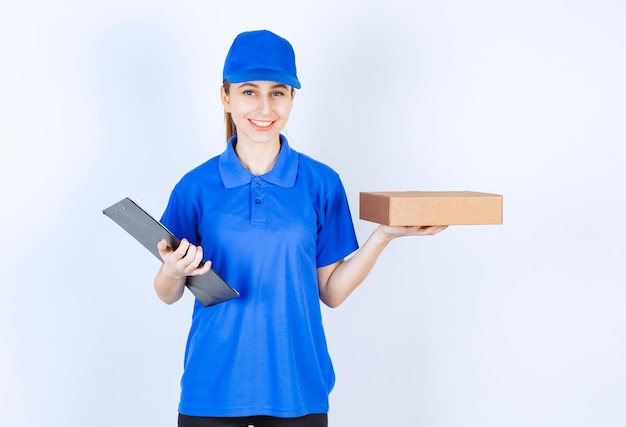 Девушка в синей форме держит картонную коробку на вынос и список клиентов.