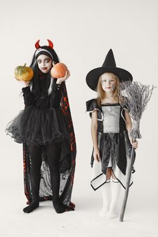 마녀로 검은 드레스를 입고 어린 소녀 옆에 서 있는 악마 의상 소녀. 소녀는 그녀의 얼굴을 피가 묻은 무서운 얼굴처럼 칠했습니다.