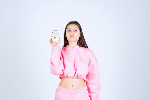 Девушка в розовой пижаме держит будильник и продвигает его как продукт. Бесплатные Фотографии