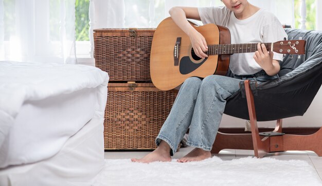 The girl is sitting and playing the guitar on the chair.