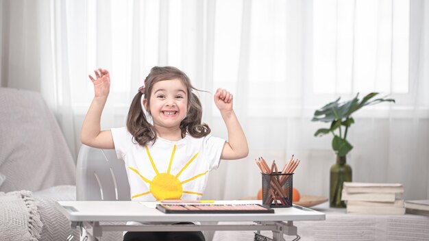 The girl is sitting at the table and doing homework. The child learns at home. Home schooling. Space for text.