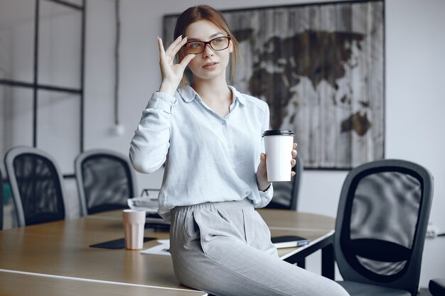 女の子がテーブルに座っています。カップを持っている女性。ブルネットがメガネを調整します。