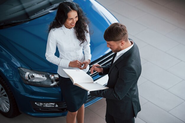 Girl is smiling. Female customer and modern stylish bearded businessman in the automobile saloon