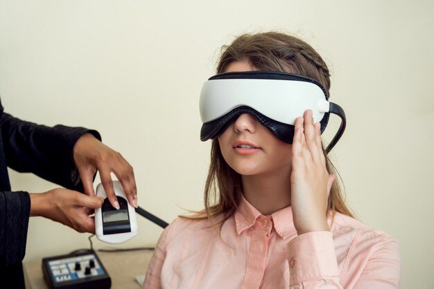 Girl is worried for her sight. Relaxed modern european woman sitting in office of eye care specialist waiting when procedure will be finished, wearing digital vision screener during check-up