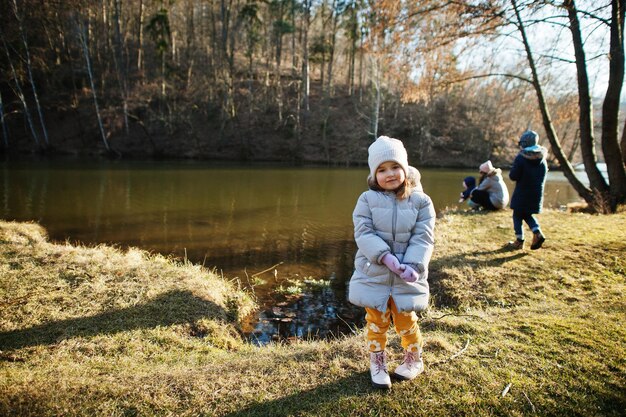 ジャケットの女の子は家族と一緒に川に対して日当たりの良い春の公園に立っています