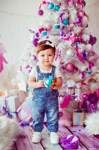 Girl in jumpers stands with toy before Christmas tree 