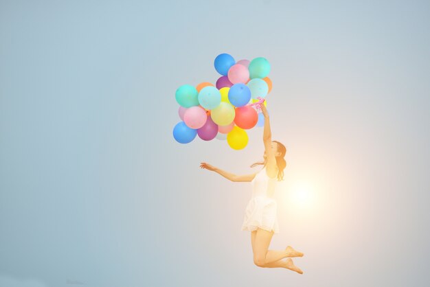 Girl jumping with balloons and sun background