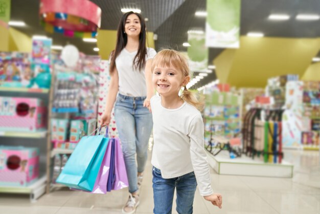 Girl keeping hand of mom and running forwardn in toy store