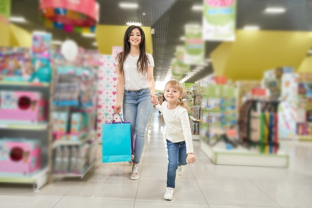 Девушка держит руку матери и бежит вперед в магазине