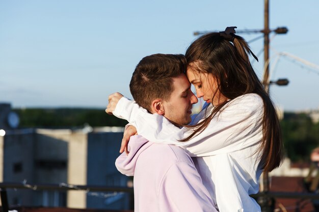 Girl kisses her man standing on the roof and watching the sunset