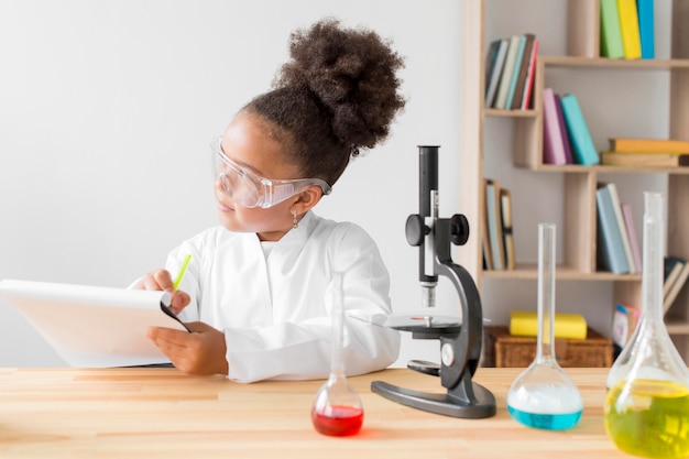 Free photo girl in lab coat and safety glasses holding notepad