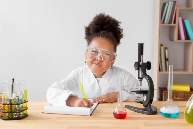 Girl in lab coat and safety glasses writing in notepad