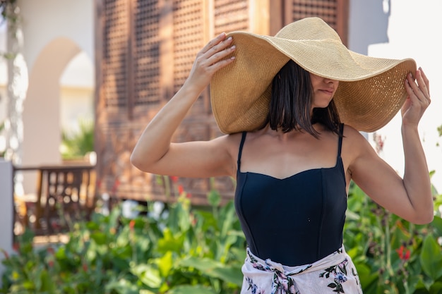 Free photo a girl in a large straw hat near the facade of an old house on a hot summer day.