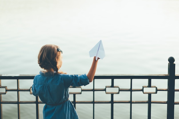 girl launching toy paper airplane looking to lake