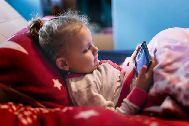 Ragazza che pone il gioco smartphone a letto