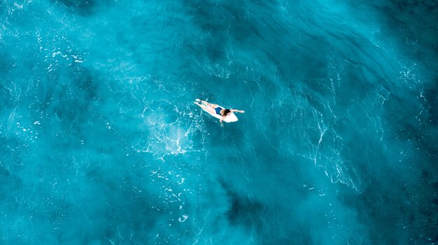 Girl laying on a surfboard and floating in the open sea with crystal clear water in Maldives