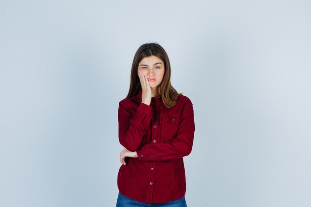 Girl leaning cheek on hand in casual shirt and looking dismal.