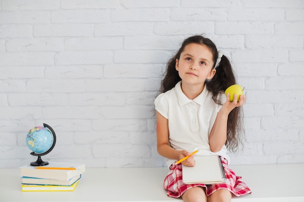 Free photo girl leaning on wall holding apple thinking