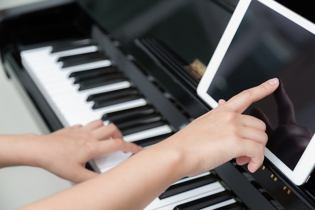 Girl learning to play the piano with a tablet