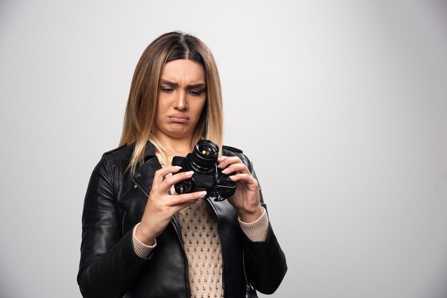 Девушка в кожаной куртке проверяет историю фотографий на камеру и выглядит недовольной.