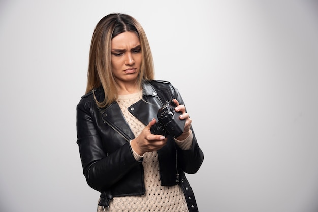 Girl in leather jacket checking photo history on camera and looks dissatisfied