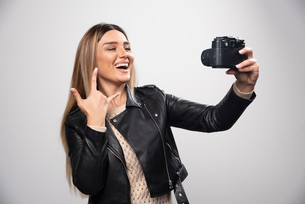 Девушка в кожаной куртке фотографирует в элегантных и позитивных позах