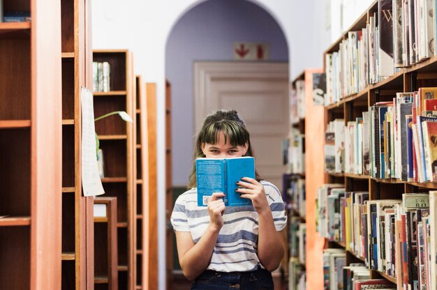 Girl in library hiding face behind a book