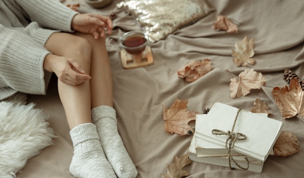 女の子は暖かい靴下、秋の気分、快適さでお茶を飲みながらベッドに横たわっています。