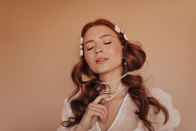 Foto gratuita ragazza in camicetta leggera pone su sfondo beige donna che tocca le sue perle di perle