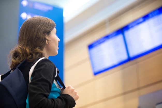 Ragazza che guarda l'aeroporto del bordo di informazioni di volo