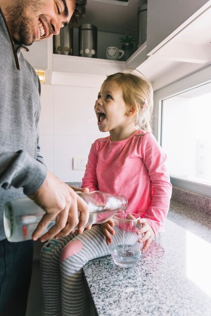 ガラスに水を注ぐ父親を見ている少女