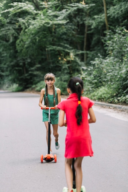 Girl looking at her friend riding scooter on road