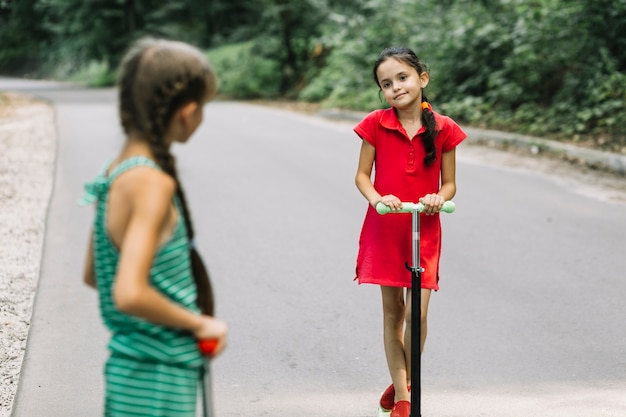 Girl looking at her friend riding scooter on road