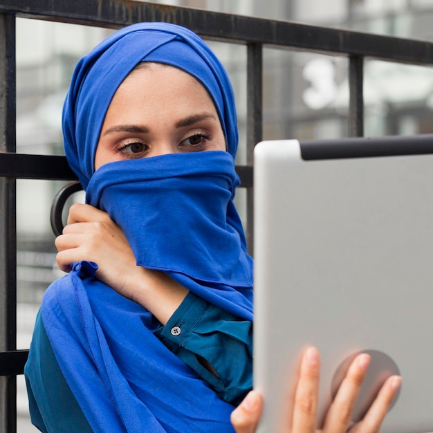 Girl looking at her tablet while covering her mouth with a hijab