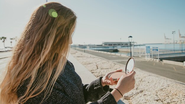 Girl looking into small mirror at harbor