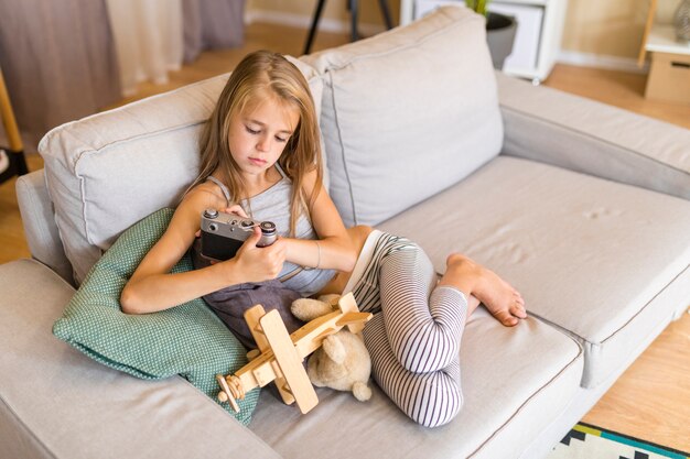 Girl looking at an old camera and sitting on couch