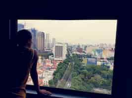 Foto gratuita ragazza che osserva dagli alberi della città città finestra