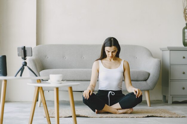 Girl looks at phone. Yogi kneading. Woman at home in a sports clothes.