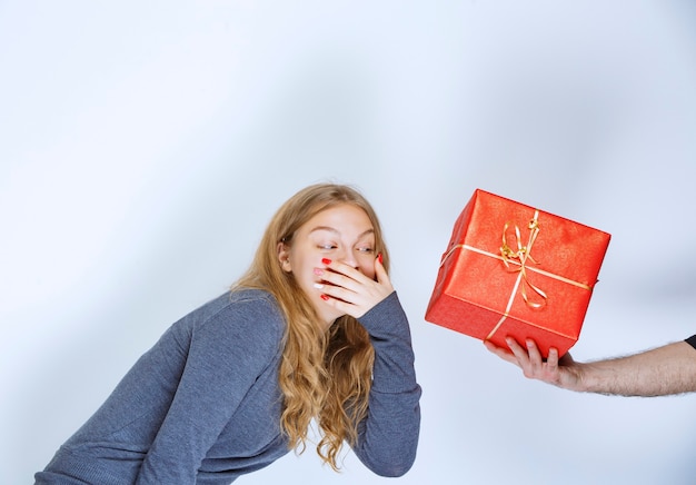 Free photo girl looks surprized as she is being offered a red gift box.