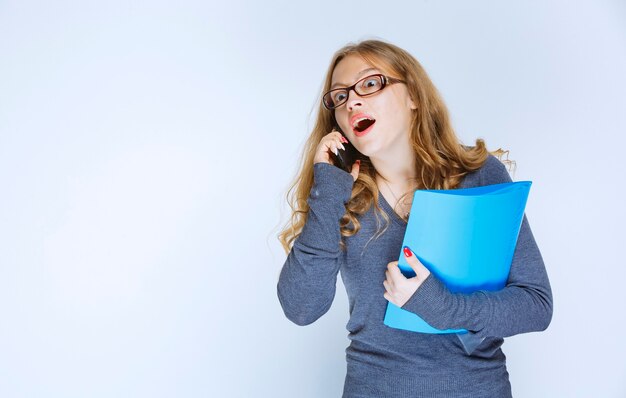 Girl looks surprized while talking to the phone and checking her reports.