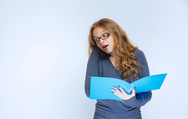 Girl looks surprized while talking to the phone and checking her reports.